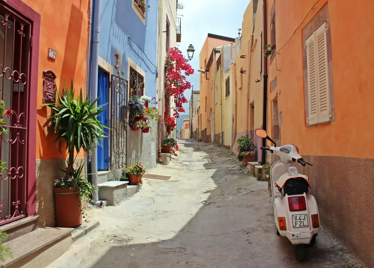 Ruelle colorée en Italie, parfaite pour une location de villa. Un scooter blanc attend, prêt pour l'aventure.