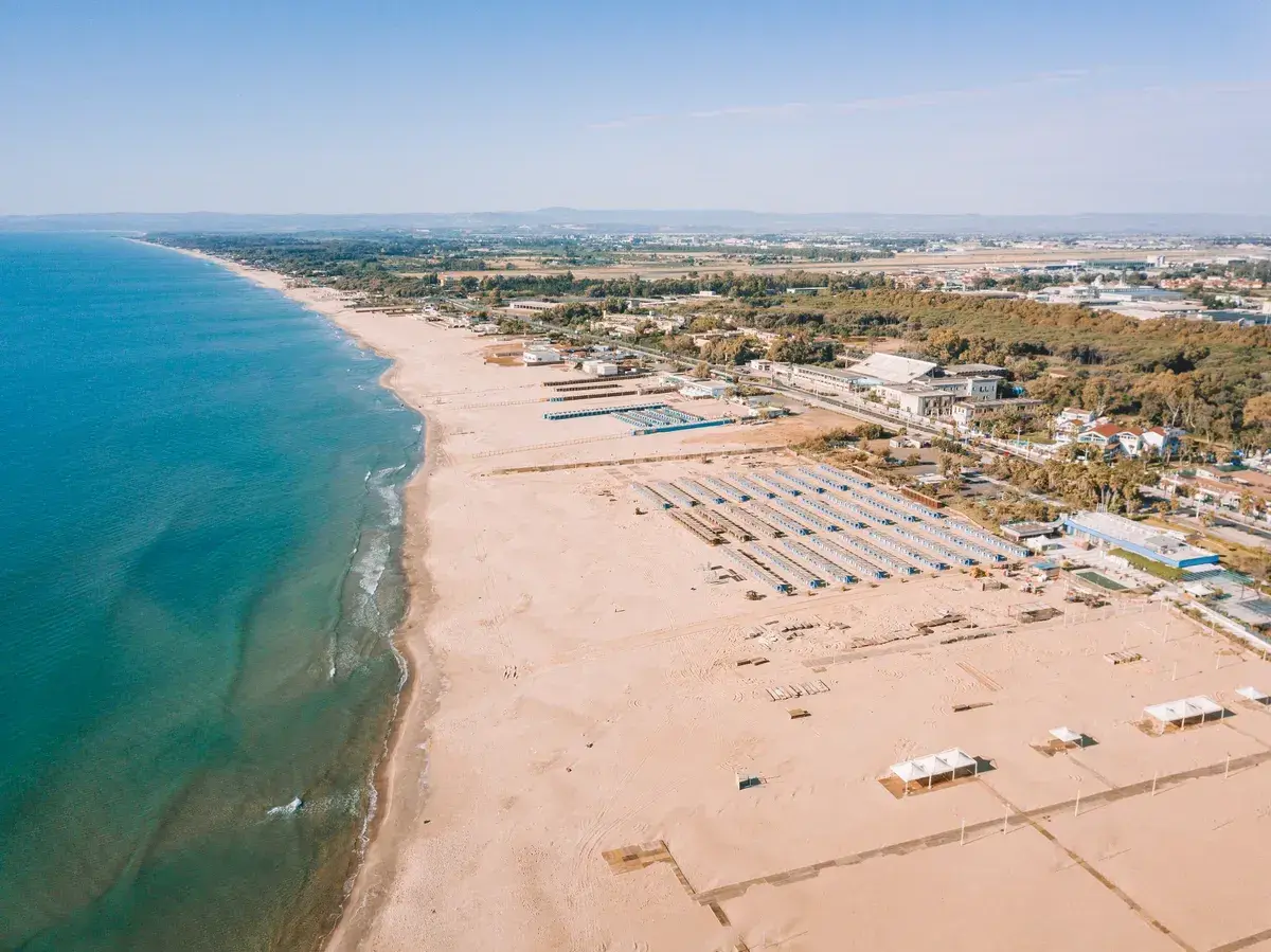 Vue aérienne d'une longue plage de sable fin bordée par la mer bleue, avec des rangées de parasols et des bâtiments à Catane, Sicile.