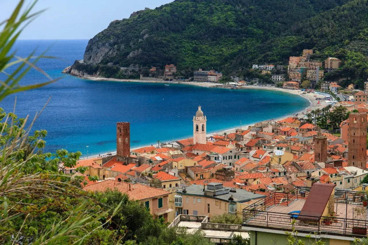 Vue d'un village pittoresque sur la côte de l'Italian Riviera, avec des maisons aux toits rouges, une plage de sable et une mer bleue étincelante.