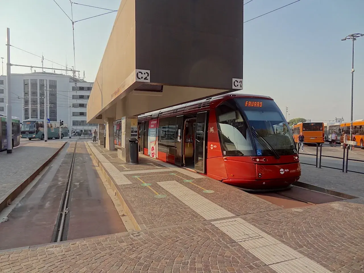 Un tram rouge moderne à Venise, prêt à partir. D'autres bus sont garés à proximité, attendant les passagers.