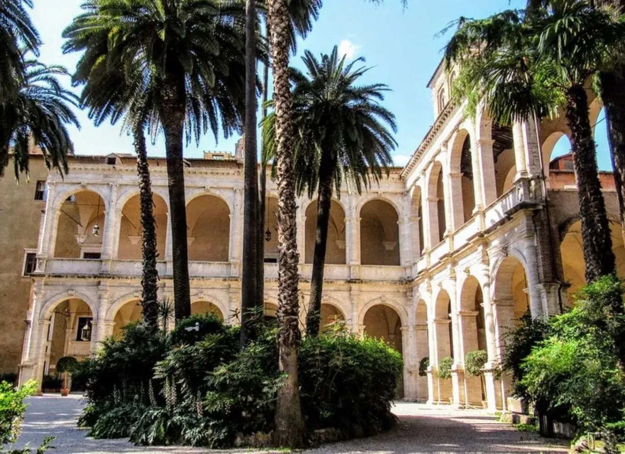 Cour intérieure avec palmiers, arcades et balcons, évoquant le Vittoriano et le Palazzo Venezia.