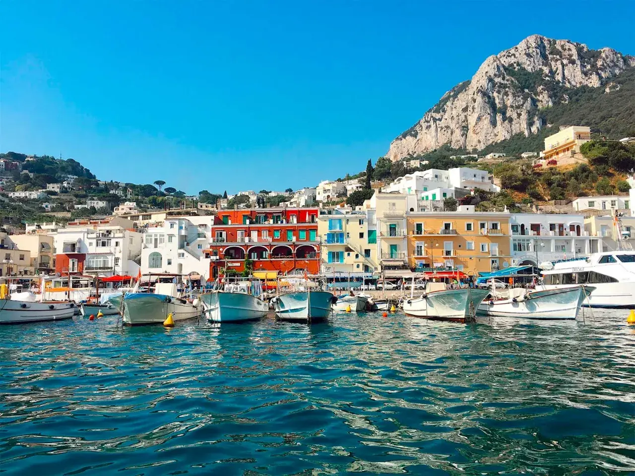 Vue du port de Capri, avec des bateaux blancs amarrés et des maisons colorées à flanc de colline. Un paysage typique de Capri, pas Ischia.