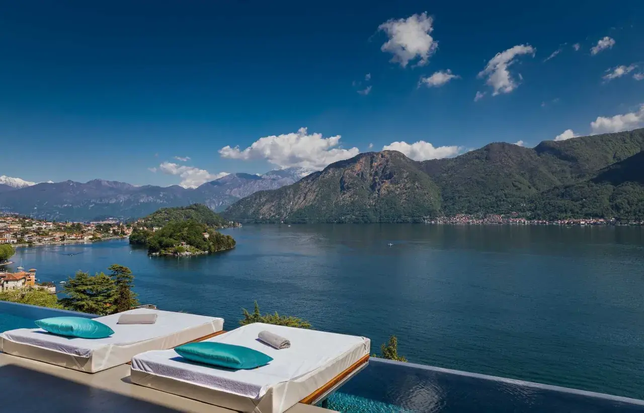 Vue panoramique sur un lac et des montagnes, avec des chaises longues et une piscine à débordement. Idéal pour des gîtes en Italie du Nord.