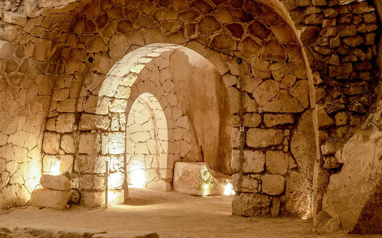 Intérieur voûté des catacombes Saint-Calixte, éclairé par des lumières douces, révélant des murs de pierres anciennes et un sarcophage orné.