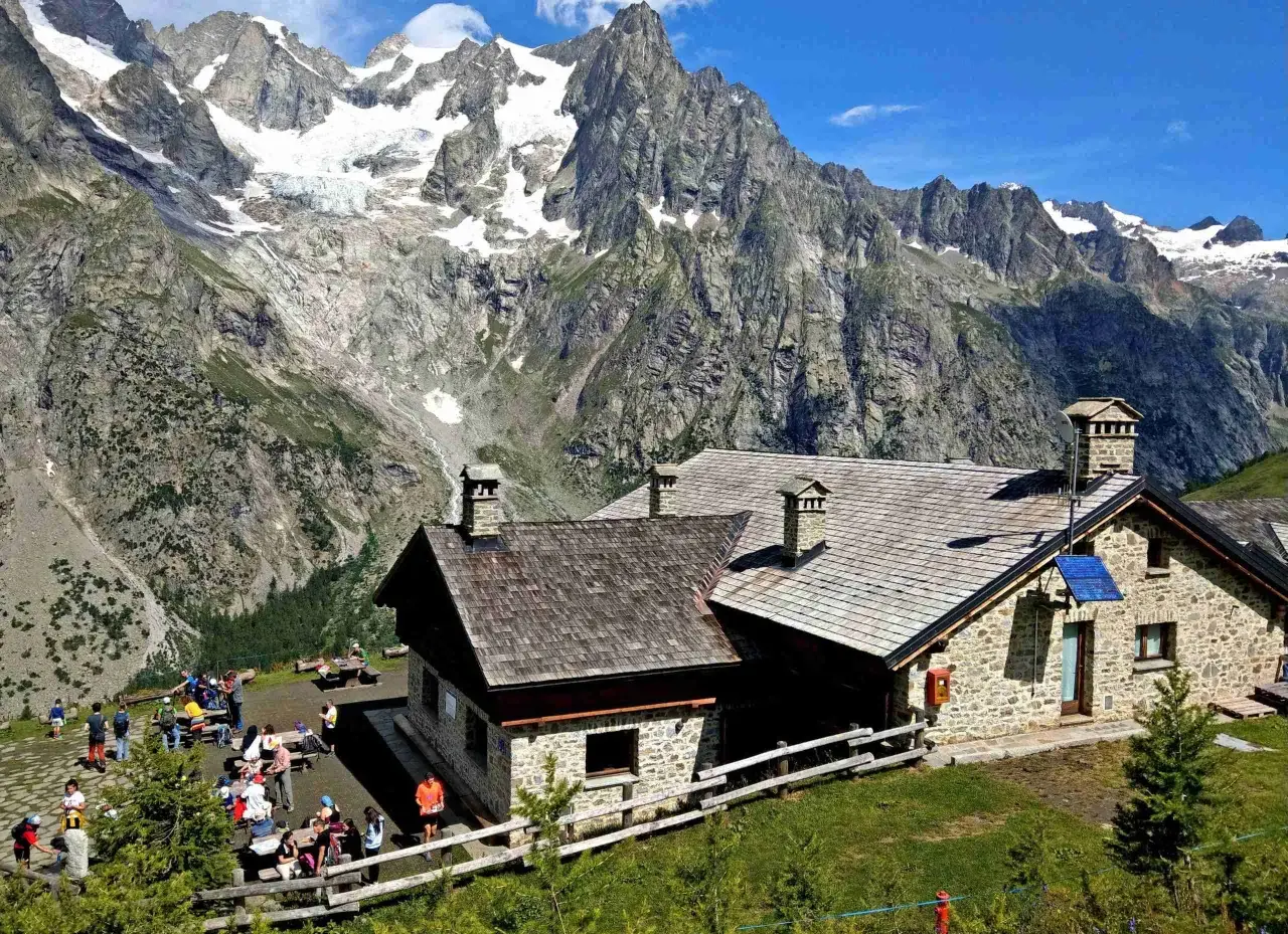 Refuge de montagne en pierre, idéal pour une location vacances Aoste Italie, avec des randonneurs profitant du paysage alpin spectaculaire.