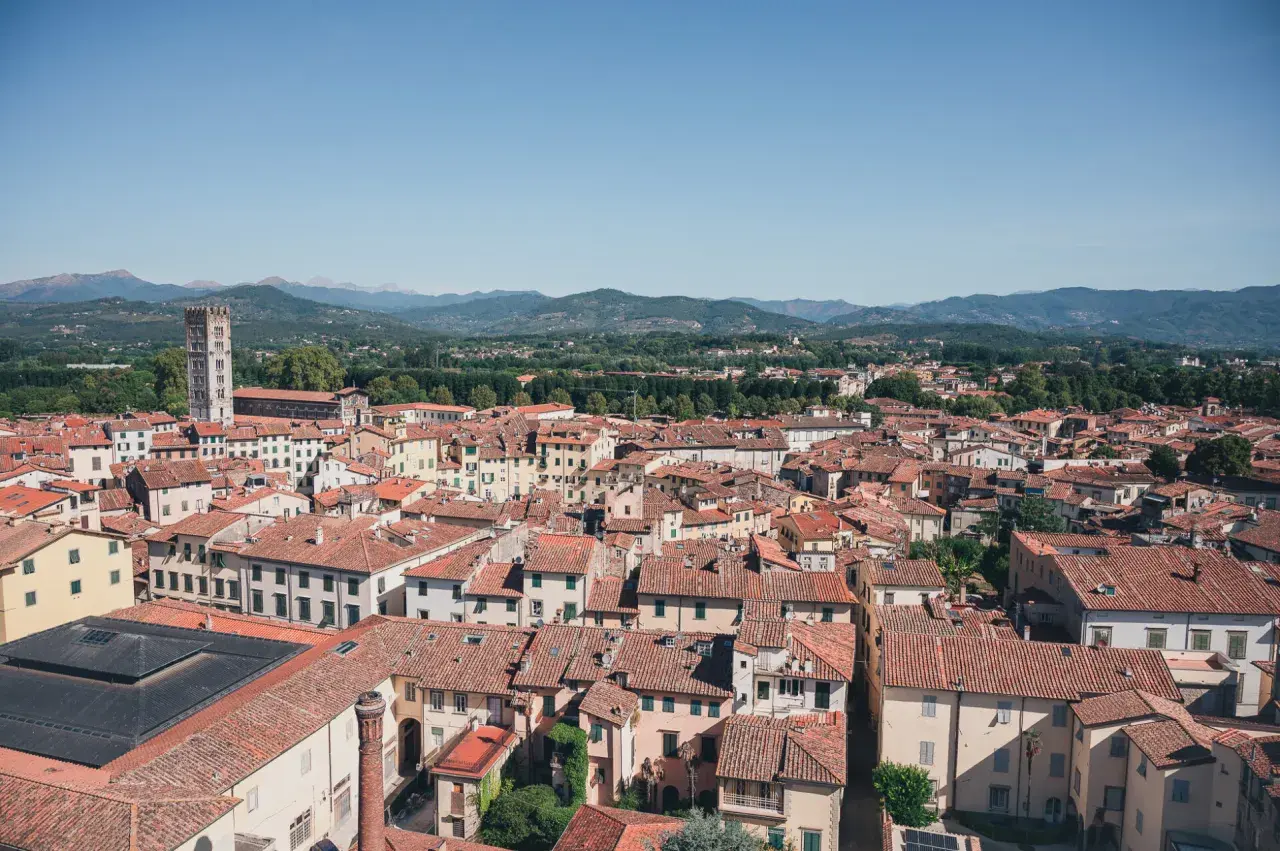 Vue aérienne de Lucques, avec ses toits de tuiles rouges et la tour de Guinigi se détachant sur les collines verdoyantes.