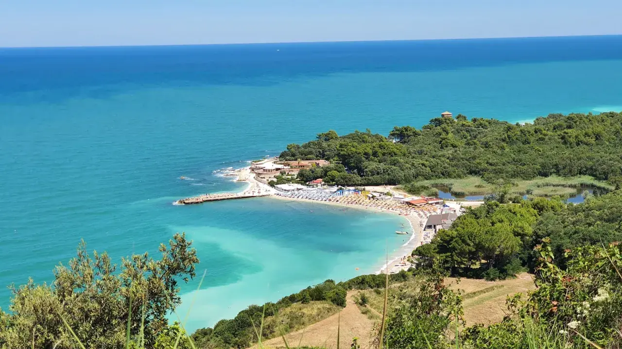 Vue panoramique de la baie de Portonovo, avec ses eaux turquoise, sa plage animée et sa végétation luxuriante.