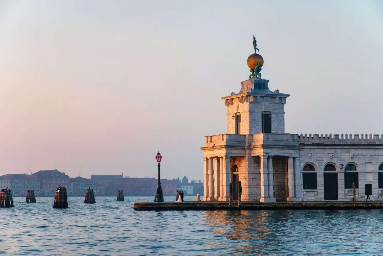 La Dogana di Venezia, un bâtiment historique, se dresse au bord de l'eau. Un couple s'embrasse près d'un lampadaire.