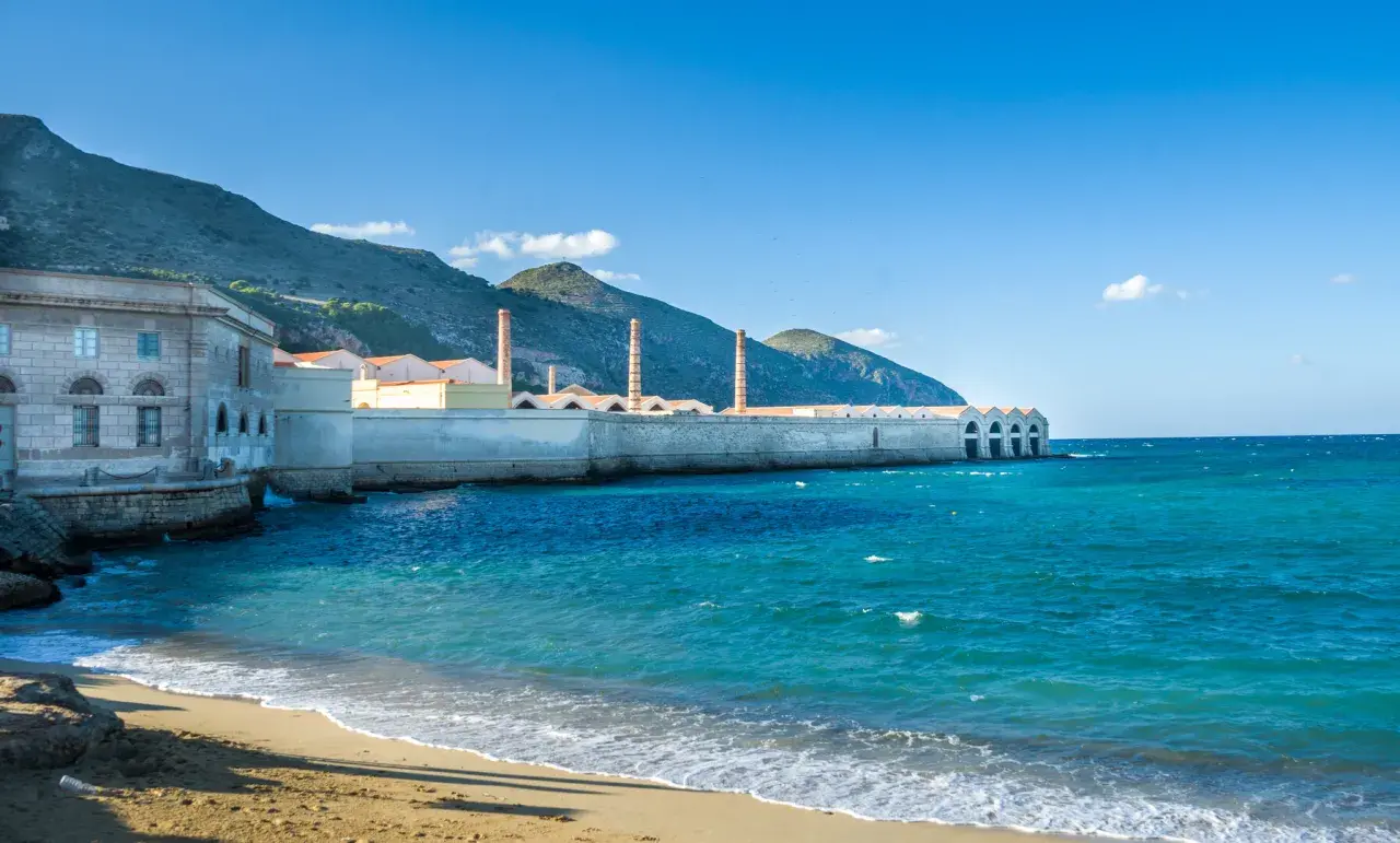 Ancienne conserverie de thon à Favignana, Sicile, avec ses cheminées emblématiques se dressant face à la mer turquoise.