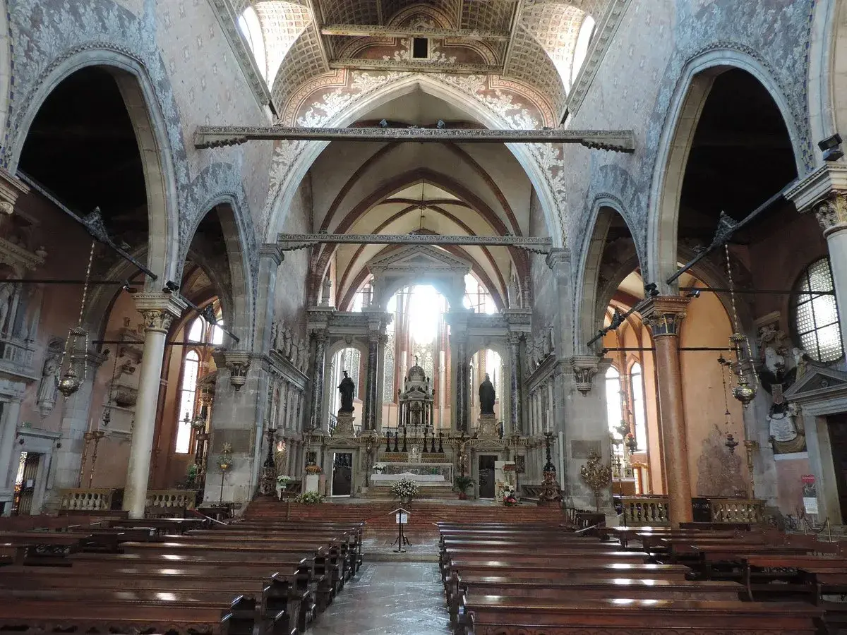 Intérieur de l'église Santo Stefano à Venise, avec ses bancs en bois, ses voûtes ornées et son autel baigné de lumière.