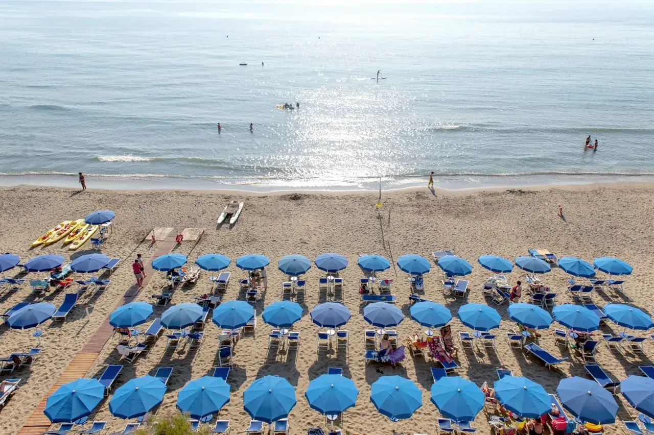 Plage de San Vincenzo en Toscane, avec des rangées de parasols bleus, des kayaks et des gens profitant de la mer.
