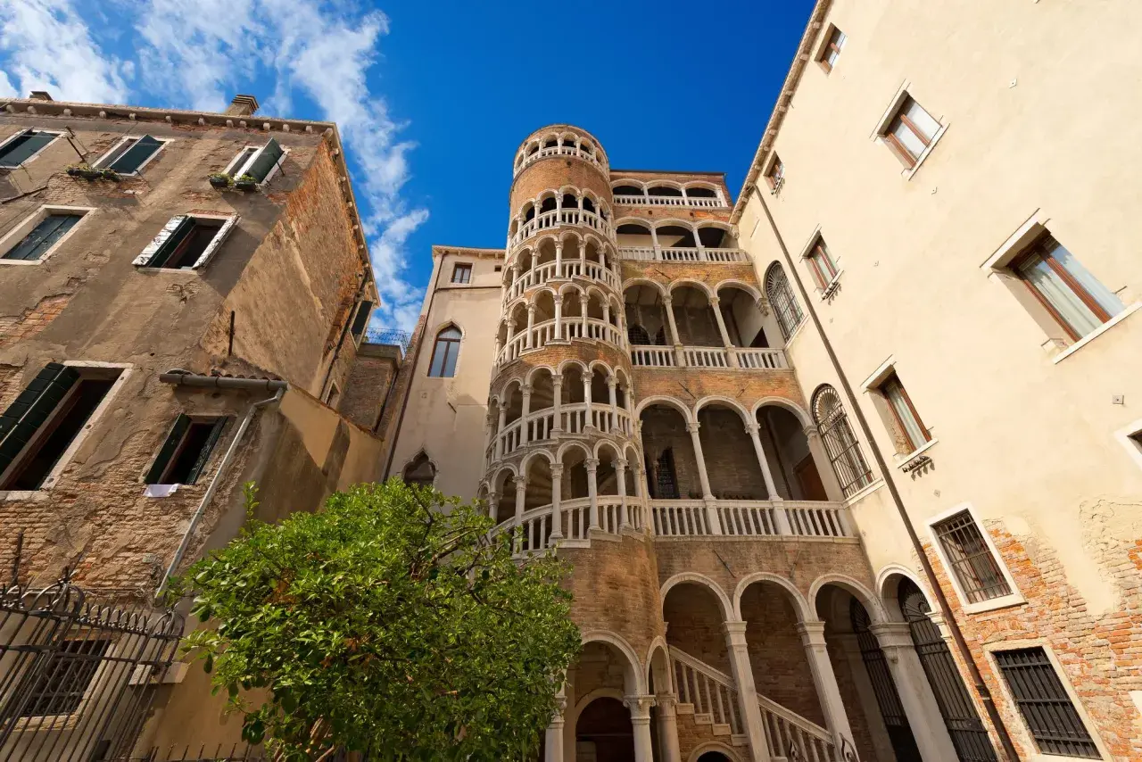 Le célèbre escalier en colimaçon du Bovolo à Venise, une merveille architecturale médiévale, se dresse fièrement sous un ciel bleu éclatant.