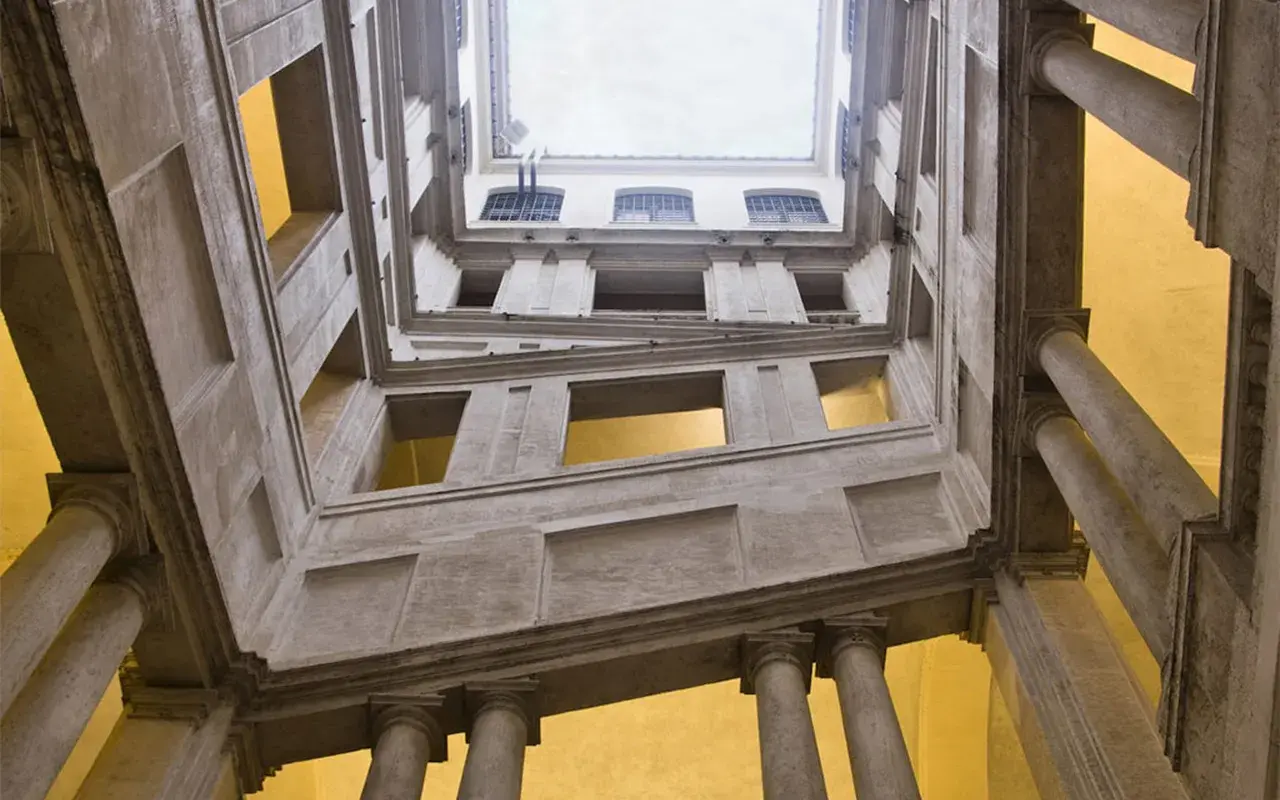 Vue en contre-plongée de l'escalier monumental du Palazzo Barberini, avec ses colonnes imposantes et ses fenêtres lumineuses.