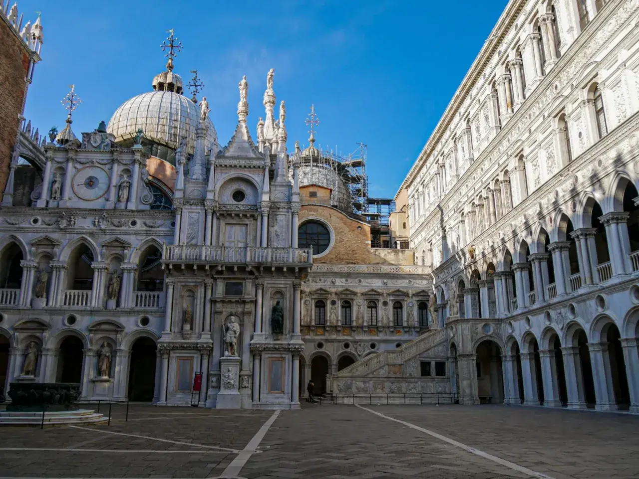 Le **Palais des Doges** à Venise, avec ses dômes, statues et arcades, se dresse majestueusement sous un ciel bleu.