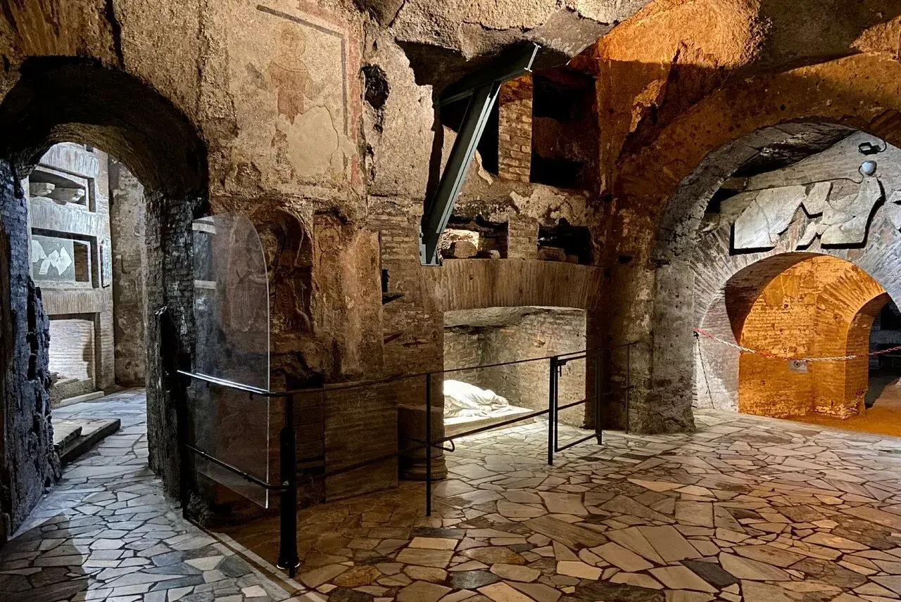 Intérieur des catacombes San Callisto. Un sarcophage blanc repose sous un arc de briques, dans un dédale de couloirs aux fresques anciennes.