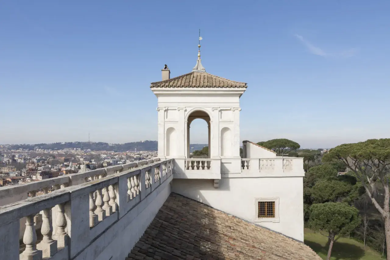Vue panoramique de Rome depuis la Villa Médicis. Un belvédère blanc orné d'une arche domine le paysage urbain.