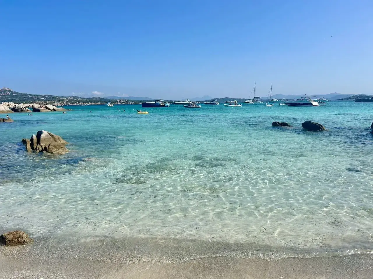 Plage de rêve en Sardaigne, eaux turquoise cristallines, rochers, bateaux au mouillage. Un coin de paradis pour savourer la ciaccia sarde.