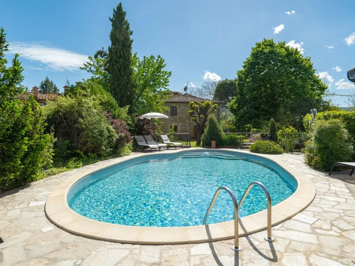Magnifique piscine dans un jardin luxuriant, typique d'une location en Toscane. Le soleil brille sur l'eau bleue, invitant à la détente.