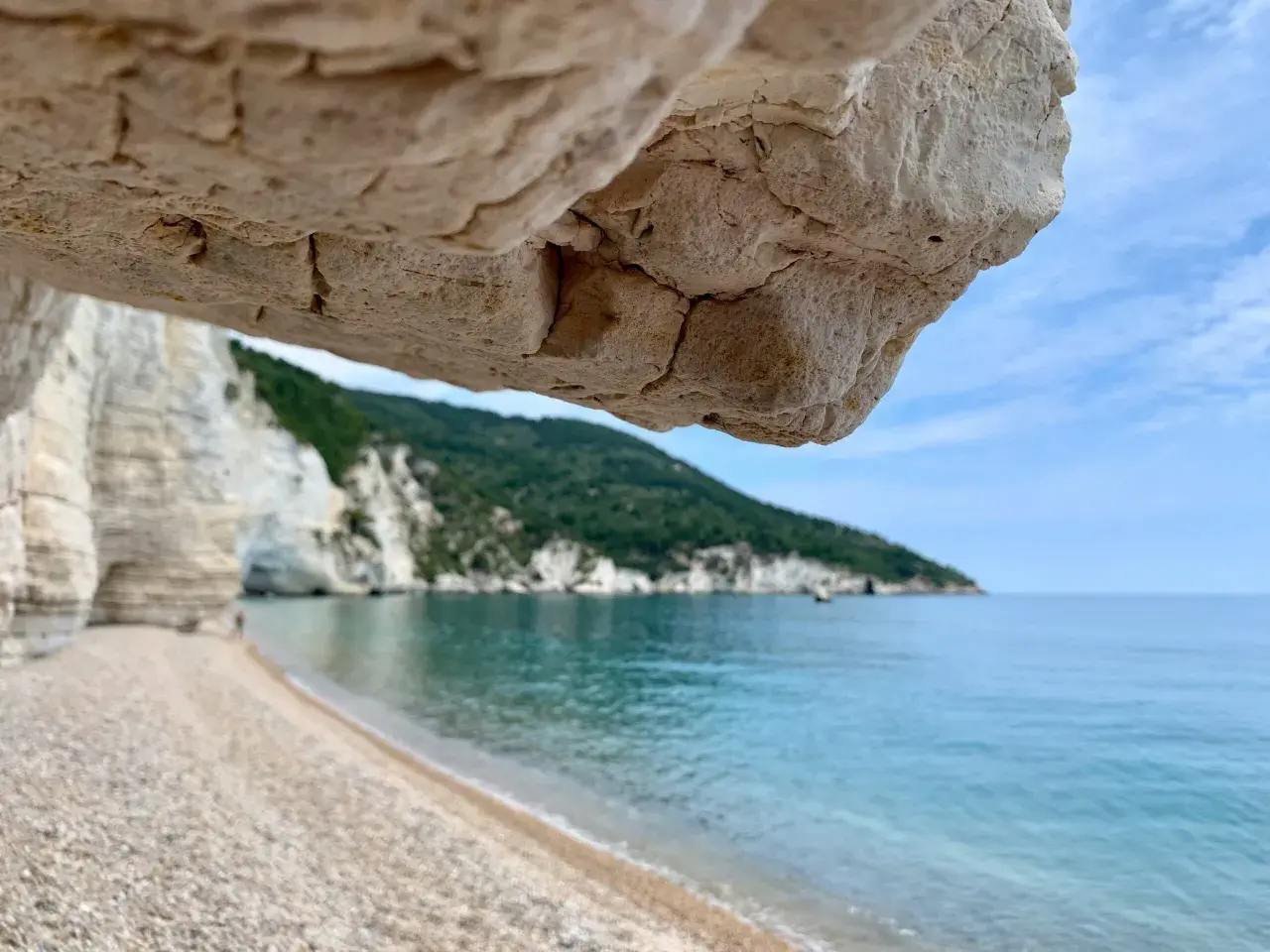 Vue depuis une grotte sur une plage de galets, mer turquoise et falaises blanches sur la côte adriatique Italie.