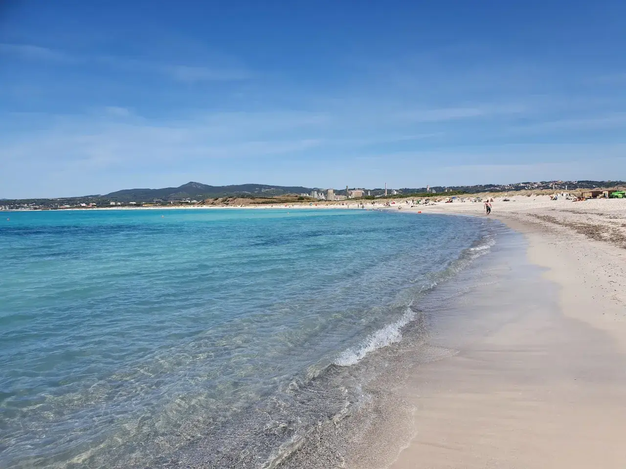 Plage de sable fin à Vada, eaux turquoise, ciel bleu, quelques personnes profitent du soleil.