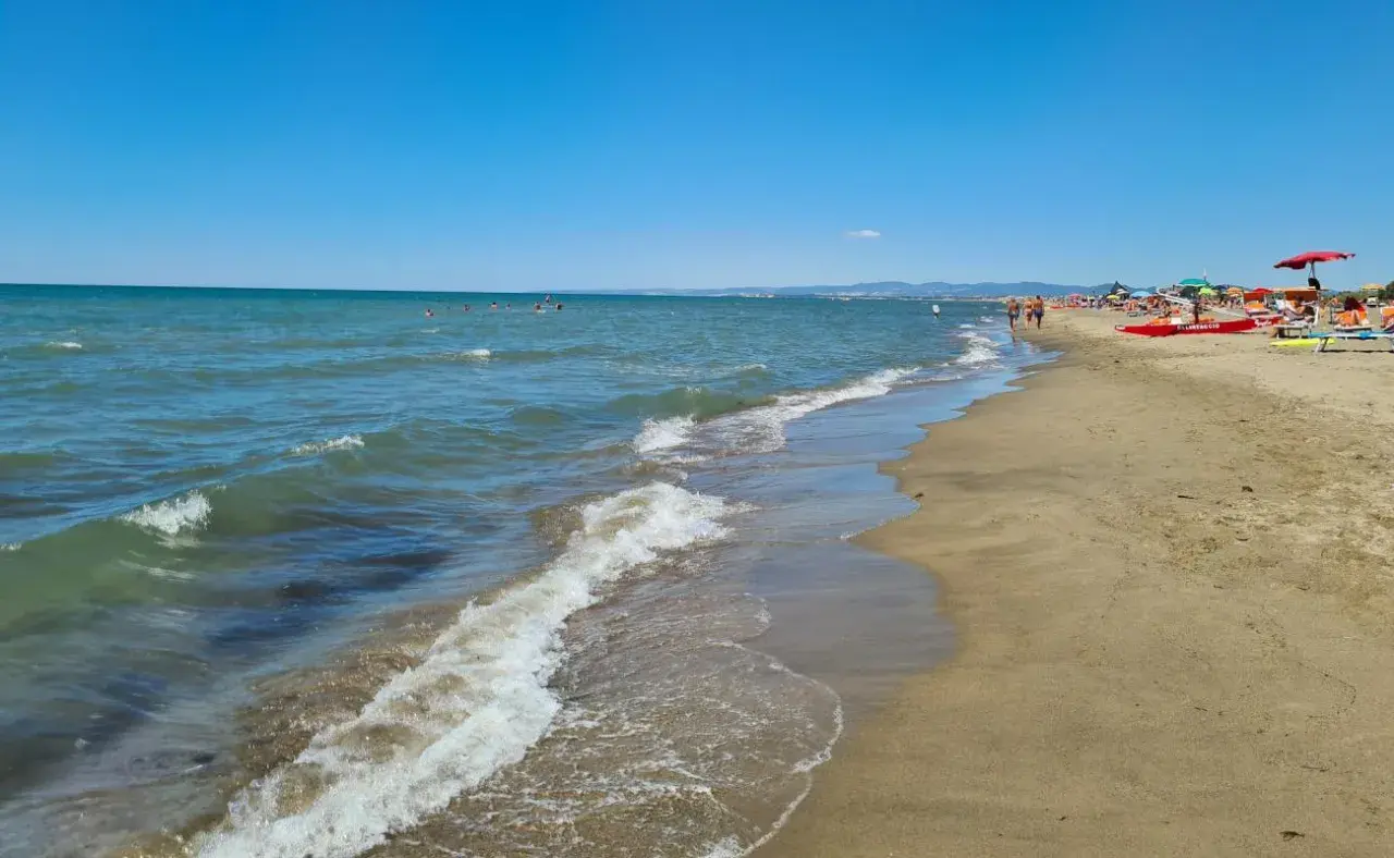 Plage de Fregene, mer bleue, sable doré, parasols et baigneurs profitant du soleil.