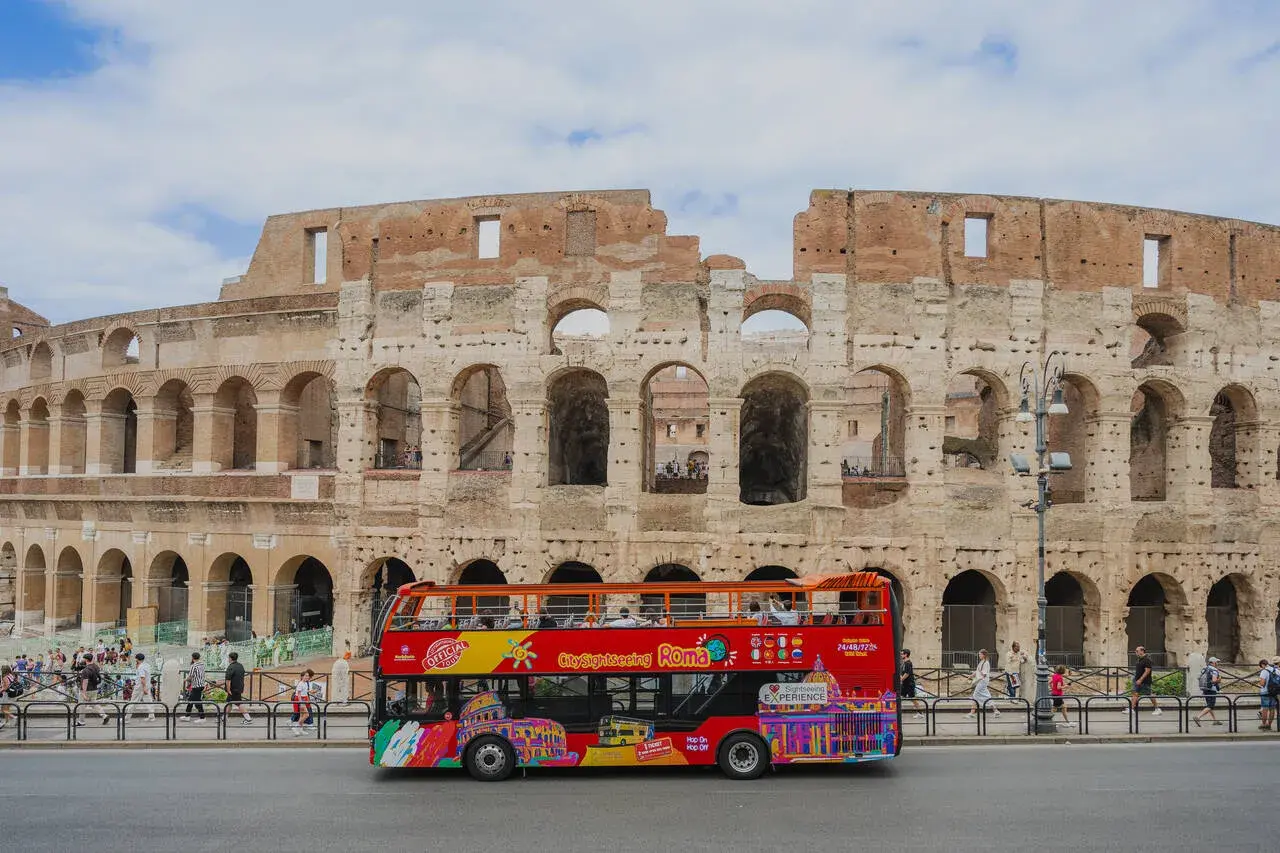 Un bus touristique rouge vif circule devant le Colisée à Rome, transportant des visiteurs pour une visite de la ville.