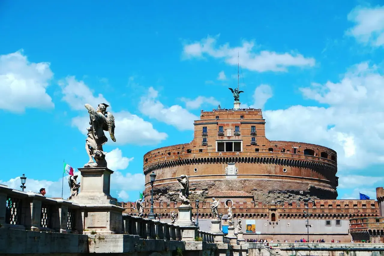 Le **château** Sant'Angelo à **Rome**, avec ses statues d'anges sur le pont, se dresse sous un ciel bleu éclatant.