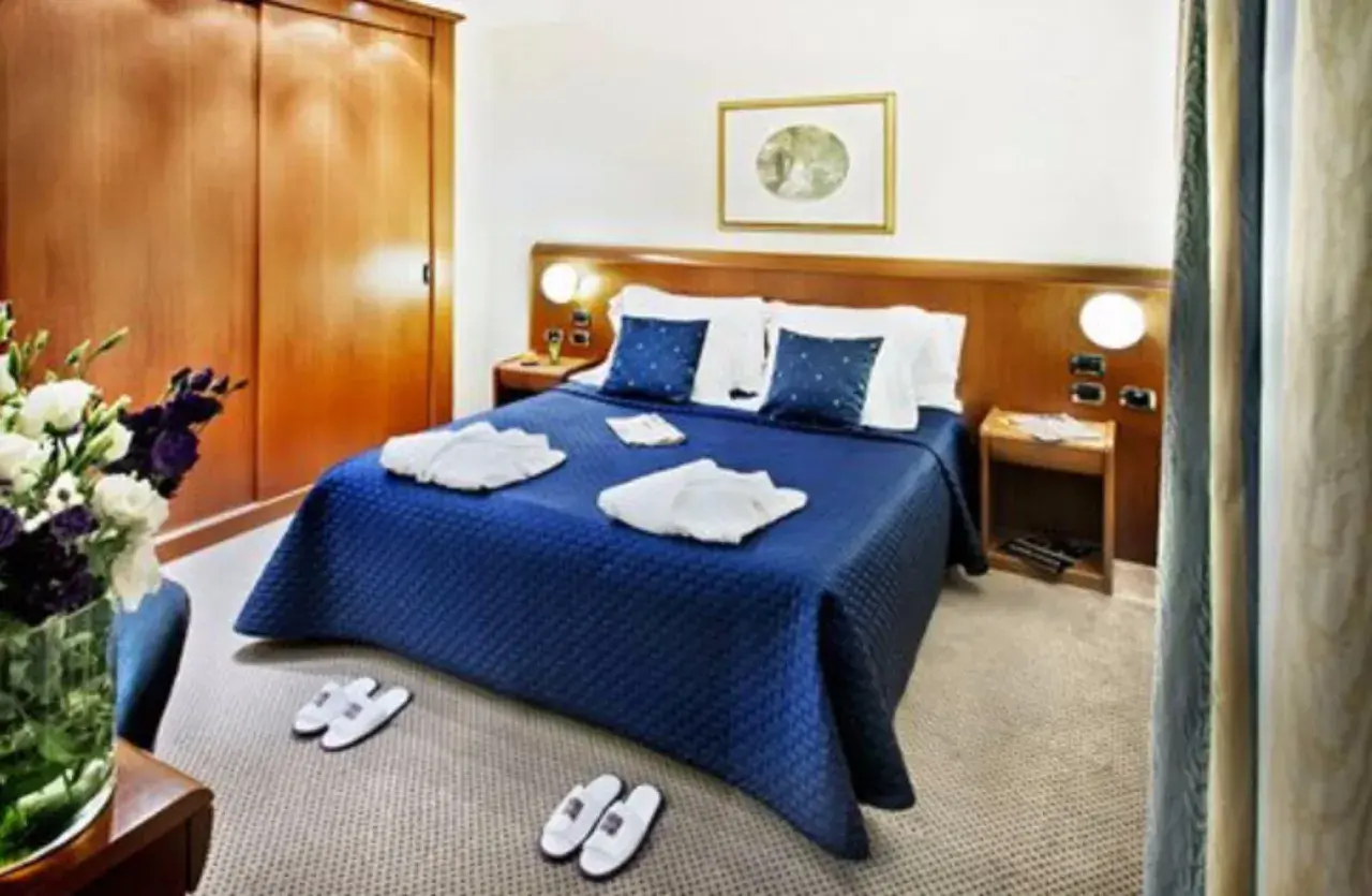 Chambre confortable à l'hôtel Ponte Sisto Rome avec lit bleu, peignoirs et pantoufles.