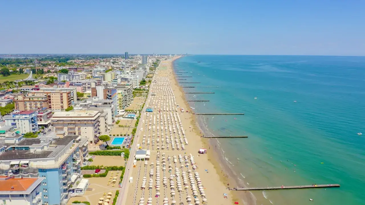 Vue aérienne de la longue plage de Lido di Jesolo, avec des rangées de parasols blancs, des hôtels et la mer Adriatique bleue.
