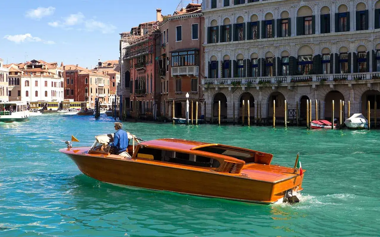 Un élégant taxi venise en bois navigue sur le Grand Canal, longeant des palais vénitiens historiques.