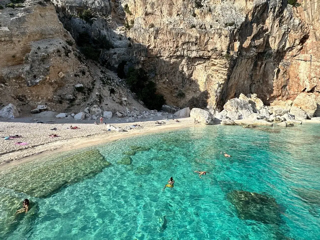 Plage de Cala Gonone en Sardaigne, eaux turquoise cristallines et falaises imposantes. Des baigneurs profitent du soleil et de la mer.