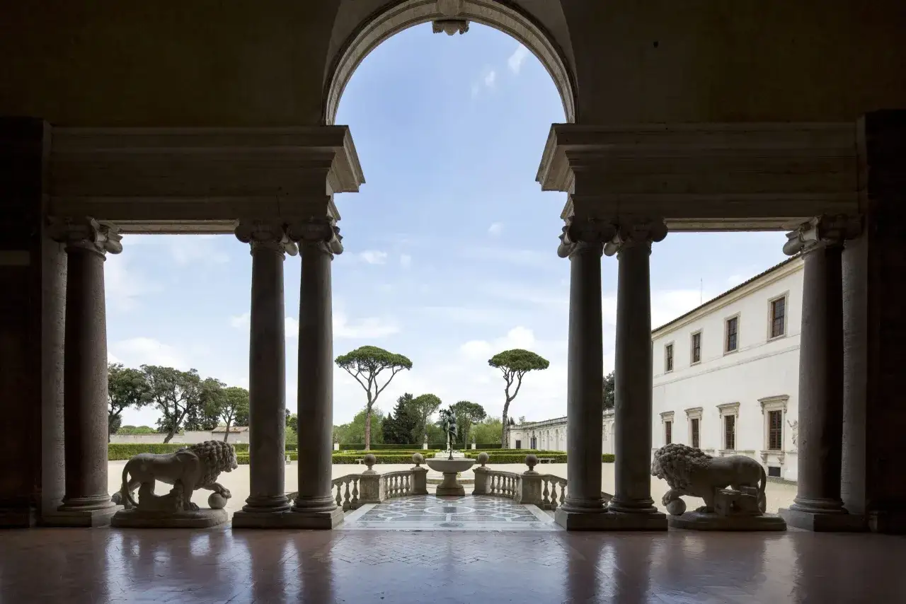 Vue d'une loggia ornée de lions de pierre, menant à un jardin avec une fontaine et des cyprès. Une belle visite de la Villa Medici à Rome.