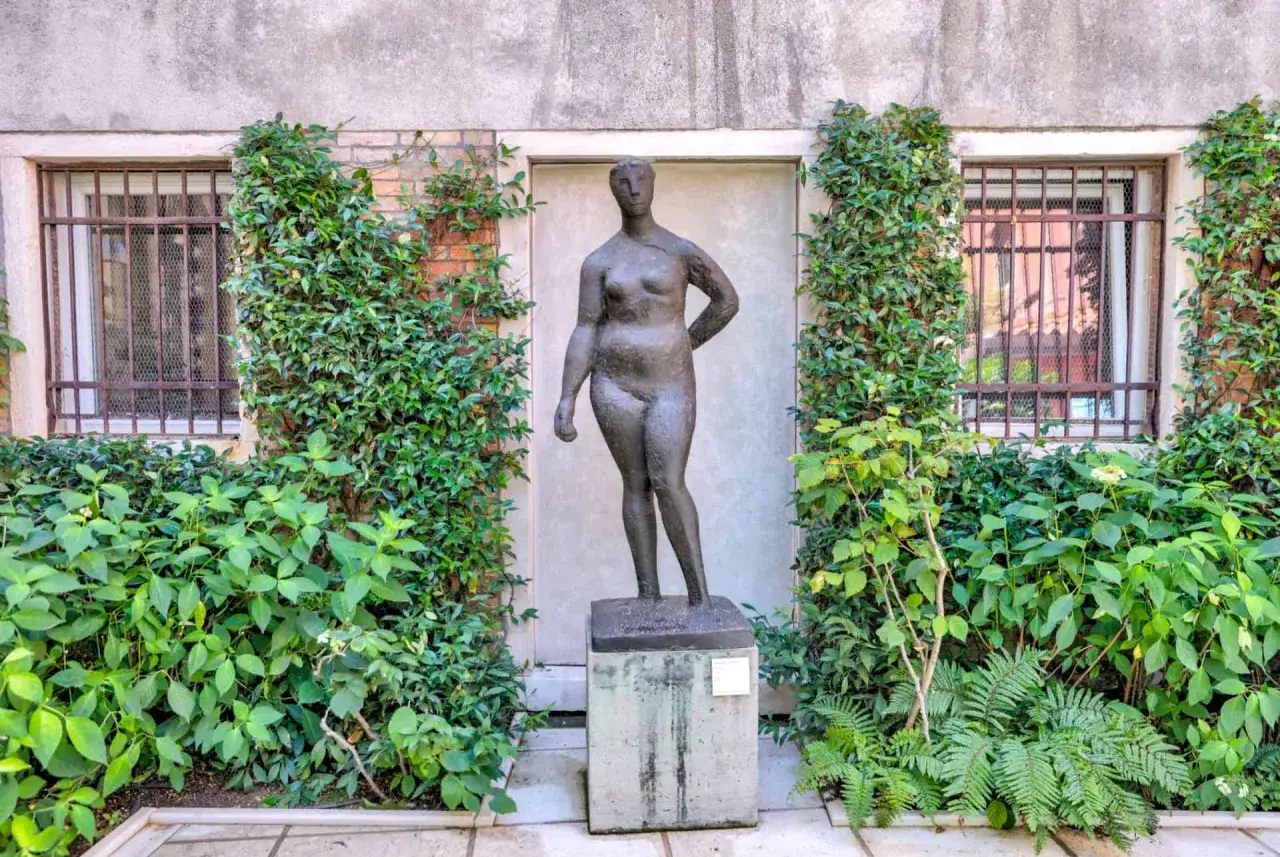 Sculpture de femme devant une fenêtre, entourée de verdure luxuriante, dans la cour du Guggenheim Venise.