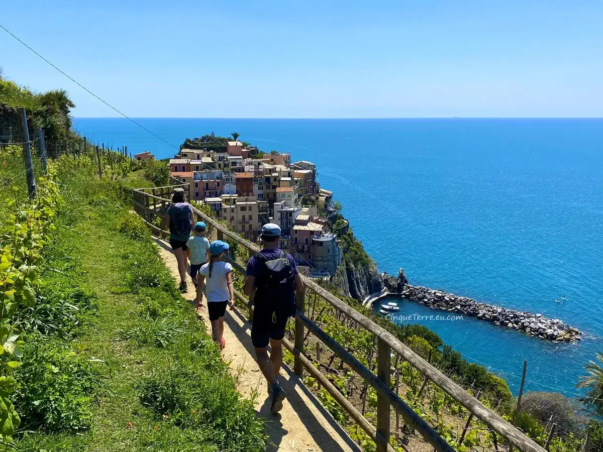 Famille en randonn&eacute;e sur le sentier de Punta Mesco, avec vue sur Manarola et la mer bleue.