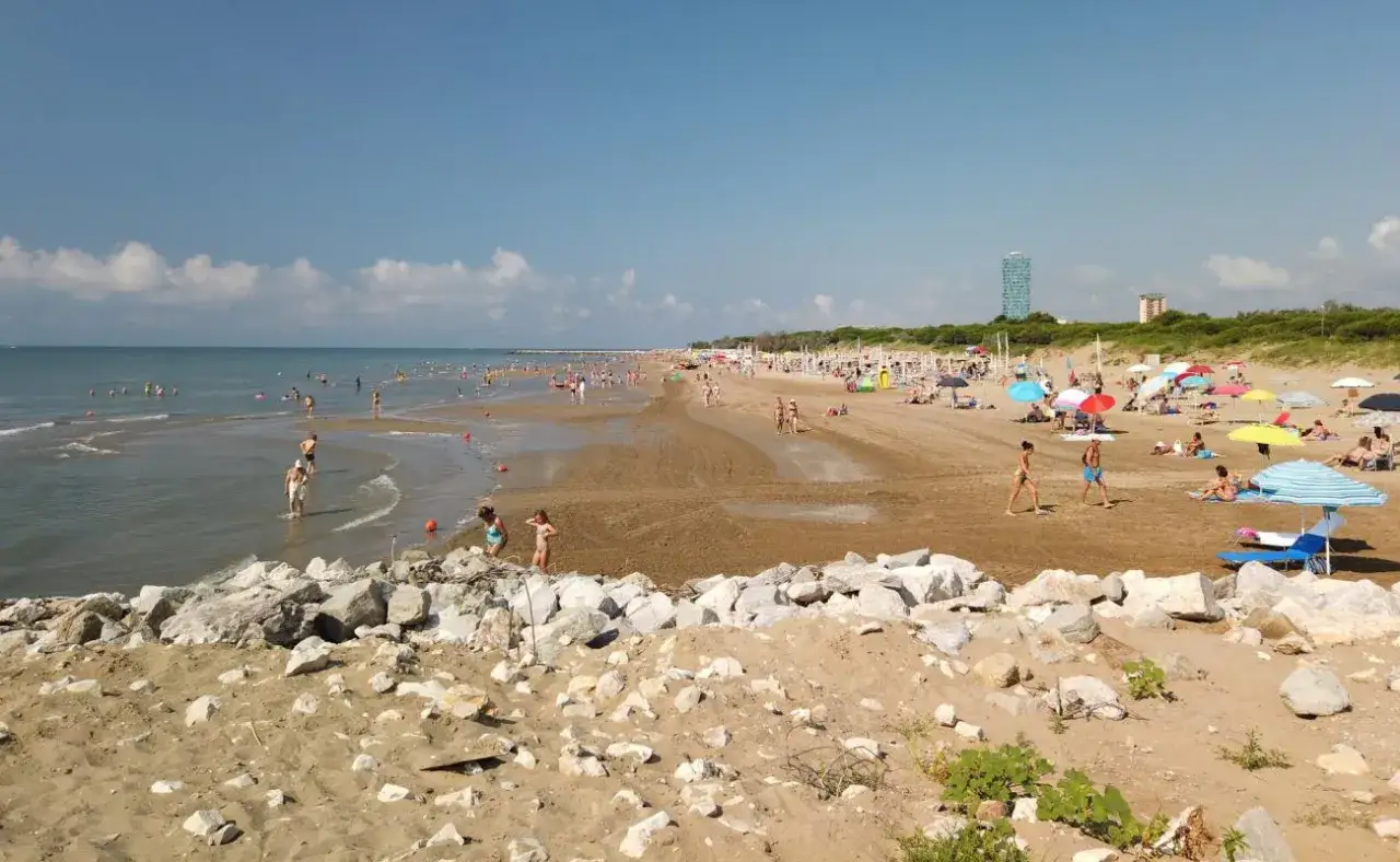 Plage animée à Lido di Jesolo, avec des baigneurs dans l'eau et sur le sable, sous des parasols colorés.