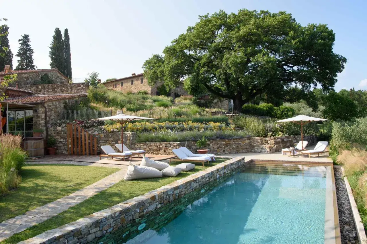 Piscine et salon de jardin dans une résidence toscane avec vue sur les collines et un grand chêne.
