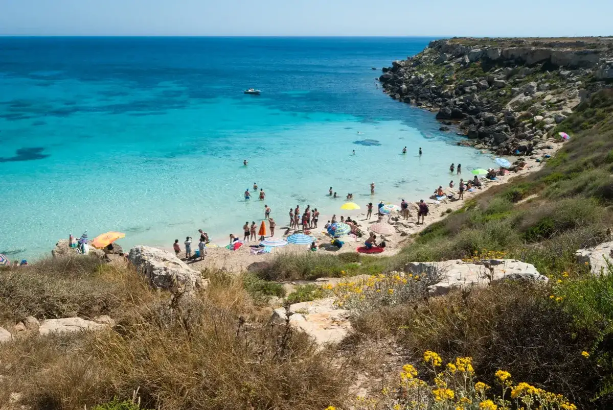 Plage idyllique à Favignana, Sicile, avec des eaux turquoise cristallines et des baigneurs profitant du soleil sous des parasols colorés.