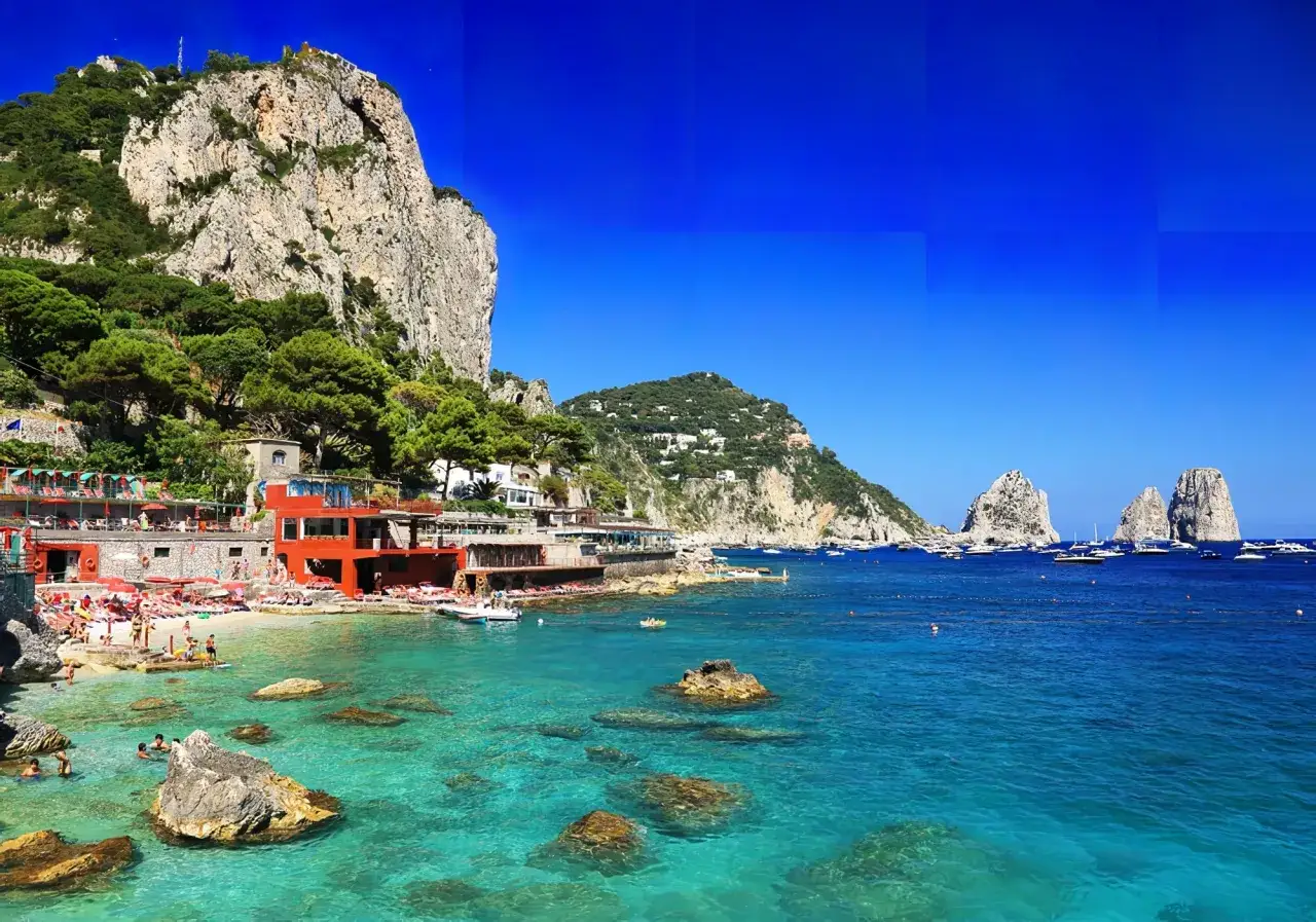 Plage animée sur une île à côté de Capri, avec des eaux turquoise cristallines, des rochers émergeant et des Faraglioni en arrière-plan.