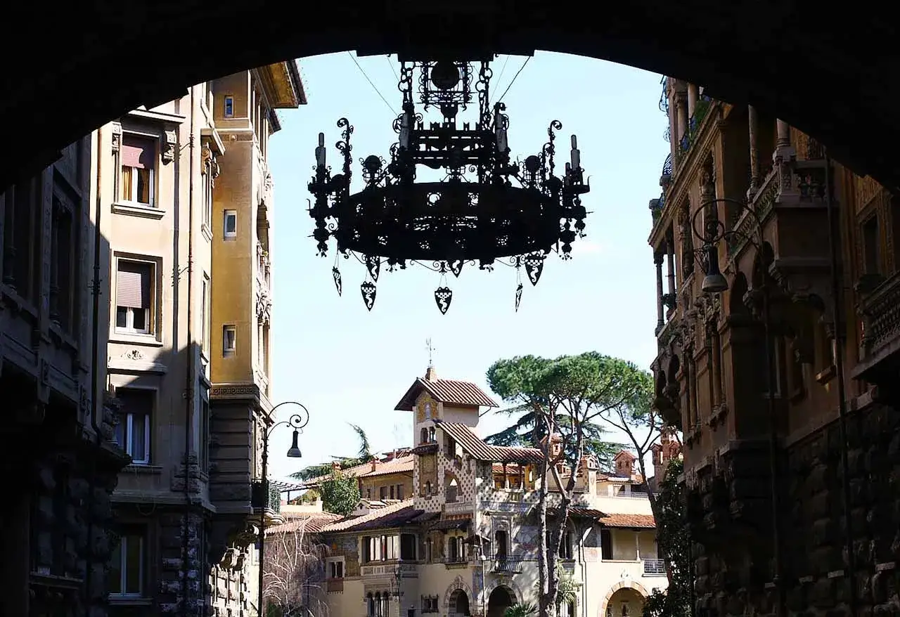 Un lustre monumental surplombe une ruelle de Rome insolite et secr&egrave;te, r&eacute;v&eacute;lant des fa&ccedil;ades orn&eacute;es et un ciel bleu.