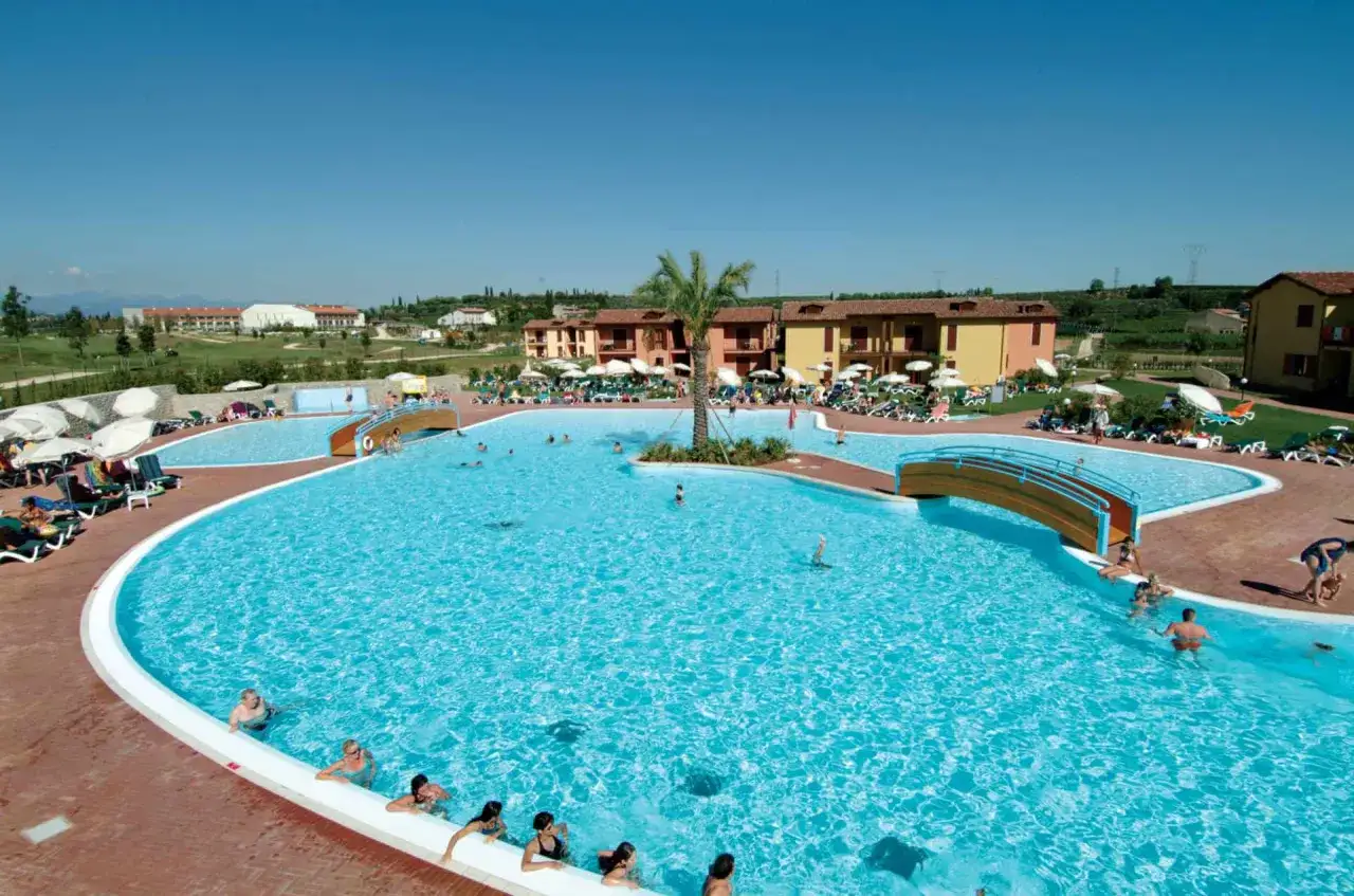 Vaste piscine d'un complexe de gîtes en Italie du Nord, avec des gens se baignant et se relaxant sous le soleil.