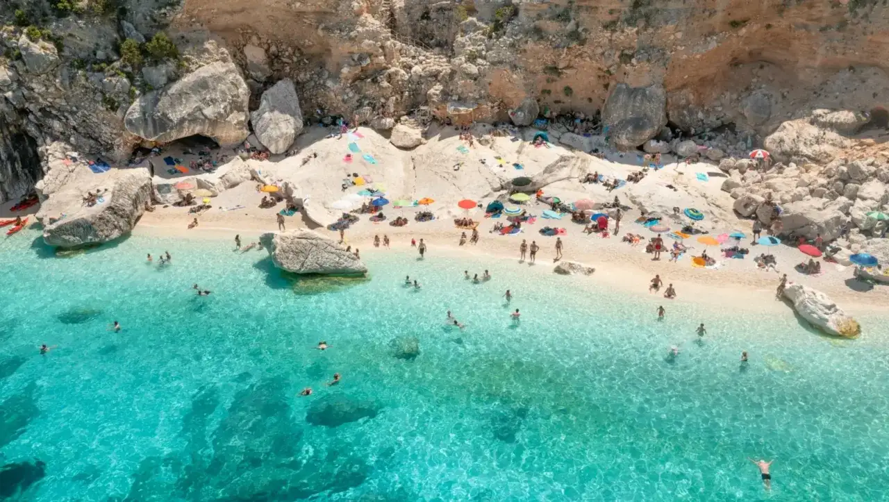 Plage italienne idyllique, eaux turquoise, rochers blancs, parasols color&eacute;s et baigneurs. Parfait pour savoir o&ugrave; partir en vacances en Italie.