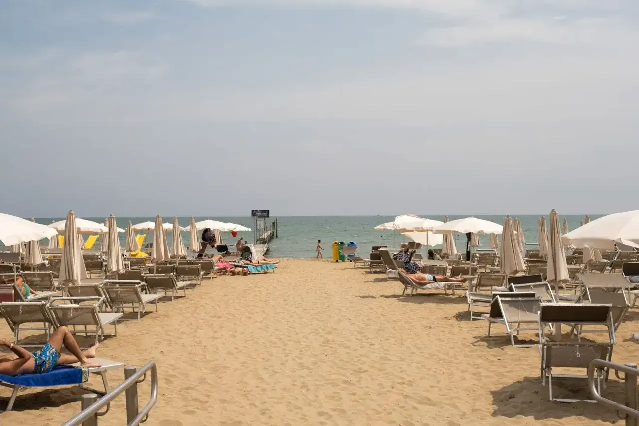 Plage de Caorle avec des parasols et des chaises longues, des gens se prélassent au soleil, une jetée mène à la mer.