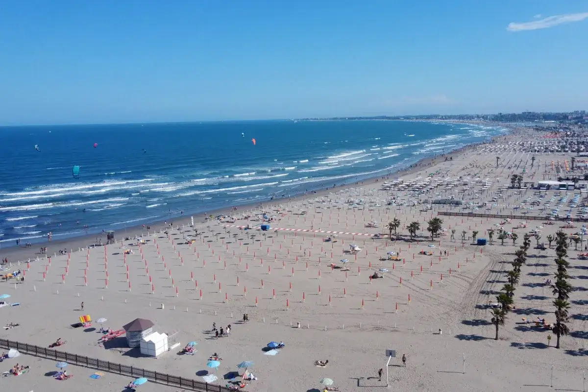 Plage animée à Chioggia, Italie, avec des parasols, des chaises longues et des kitesurfeurs sur la mer Adriatique.