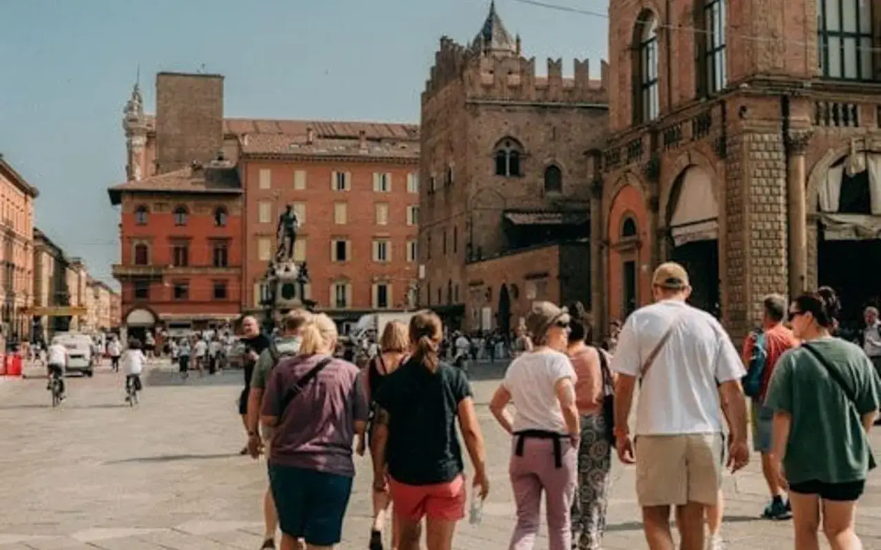 Un groupe de touristes explore une place animée de Bologne, avec des bâtiments historiques et une statue. Idéal pour visiter Bologne en 1 jour.