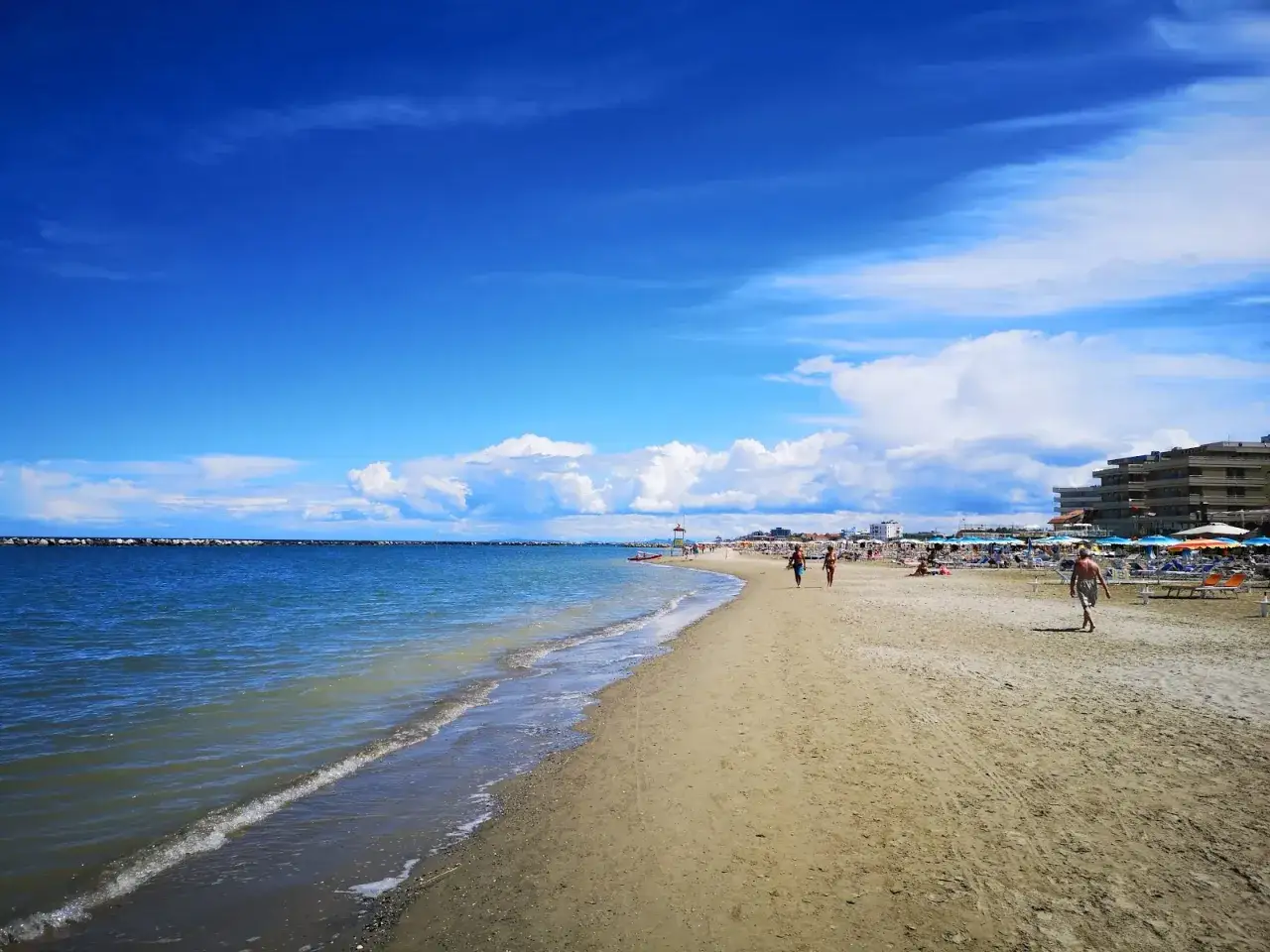 Plage animée à Gatteo Mare sous un ciel bleu éclatant. Des vacanciers profitent du soleil sur le sable doré, tandis que les vagues douces caressent le rivage.