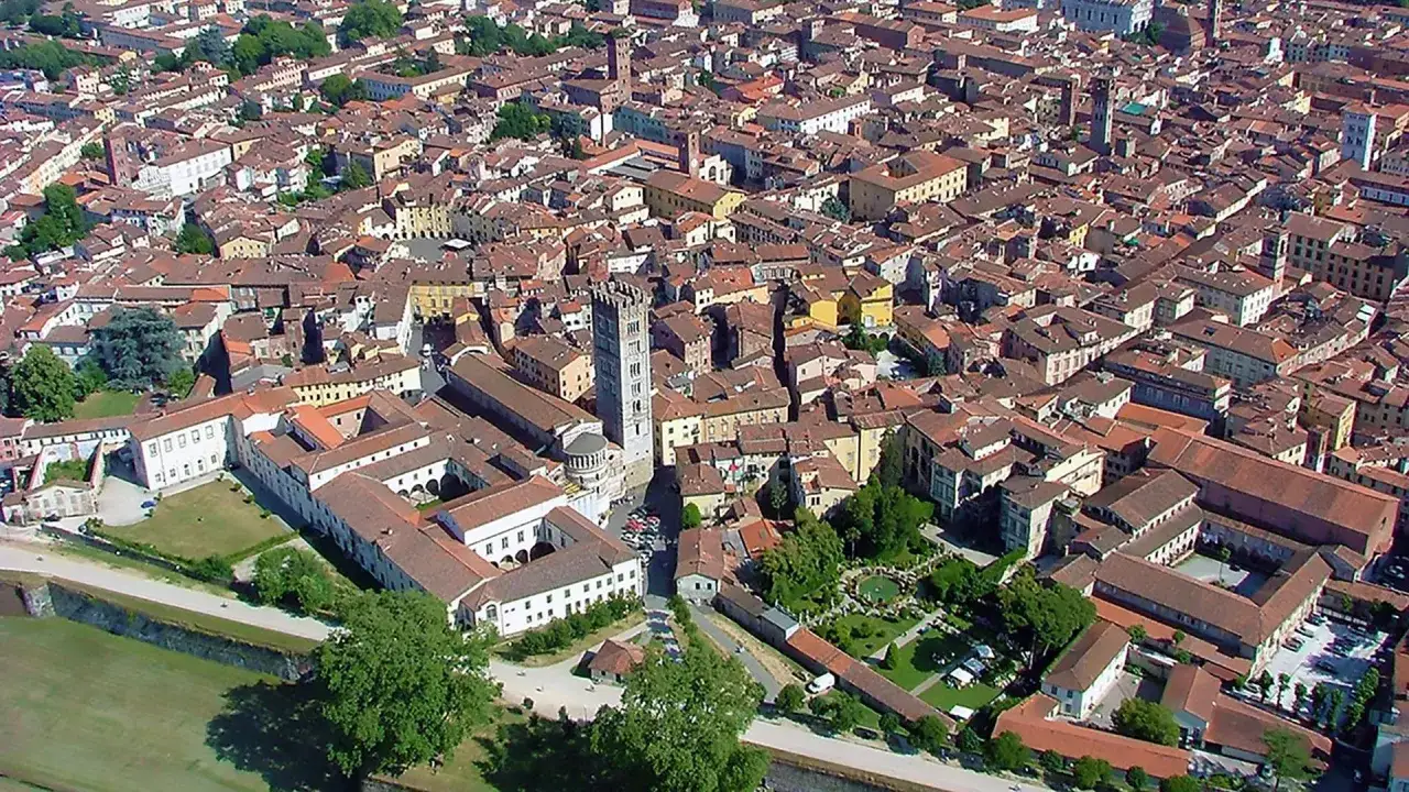 Vue aérienne de Lucca, avec ses toits de tuiles rouges et la tour Guinigi. Un parking est visible près de la cathédrale.