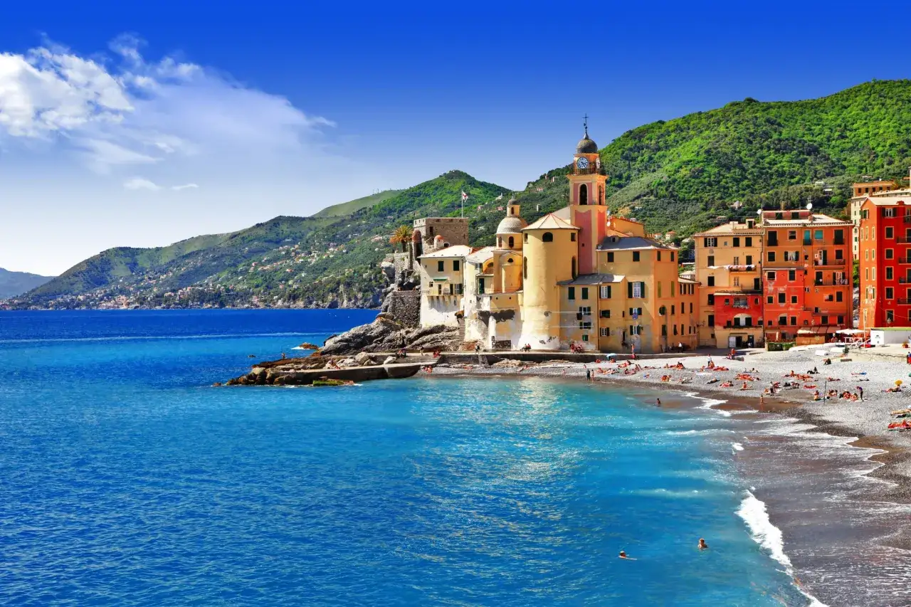 Plage animée à Camogli, Ligurie, avec des maisons colorées perchées sur la falaise et des eaux bleues scintillantes.