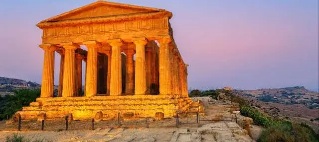 Temple de la Concorde à Agrigente, Sicile, baigné par la lumière dorée du crépuscule. Un vestige antique majestueux sur fond de ciel pastel.