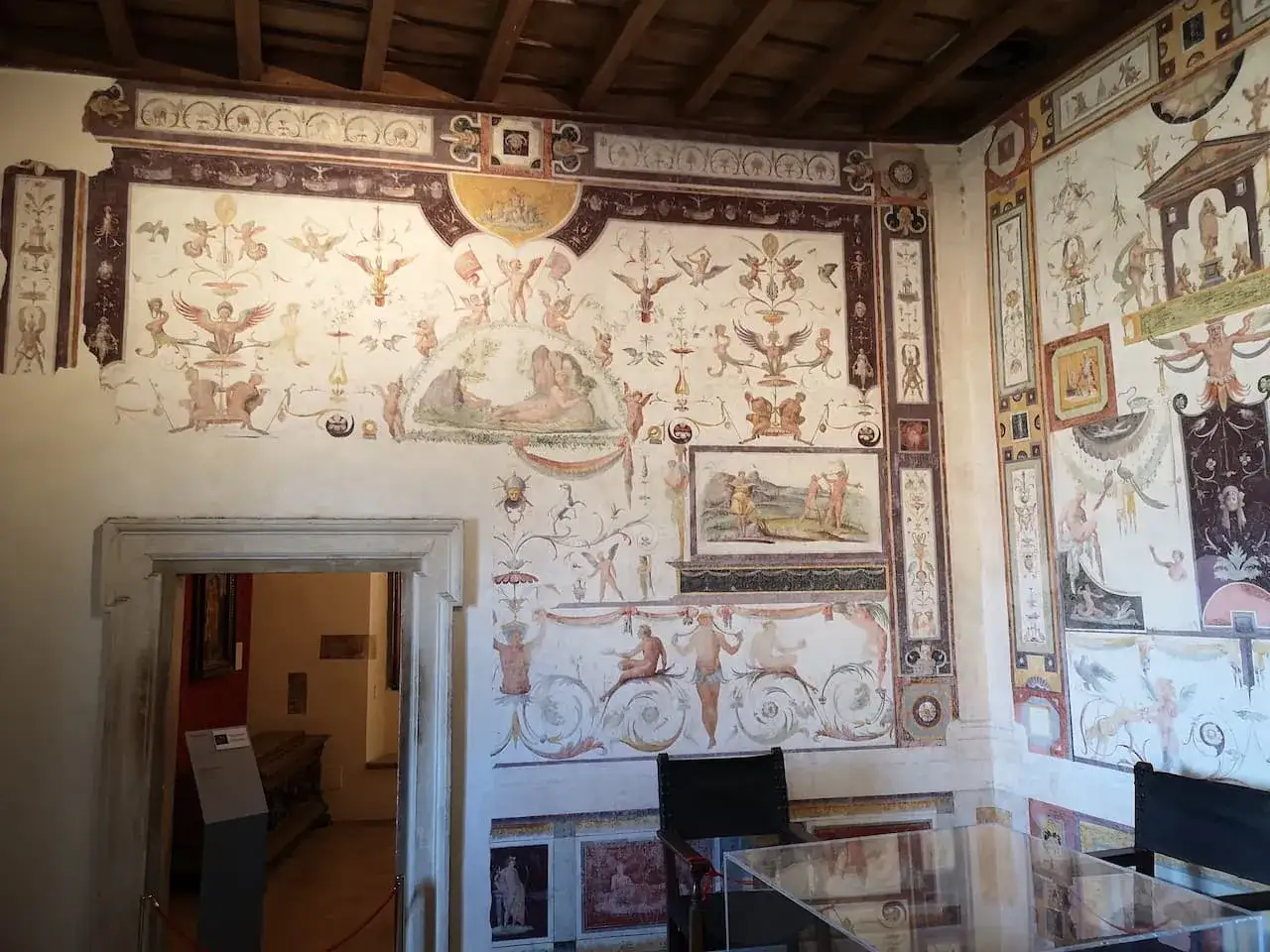 Intérieur du château Saint-Ange : fresques mythologiques ornant les murs d'une pièce, avec une porte ouverte sur une autre salle.
