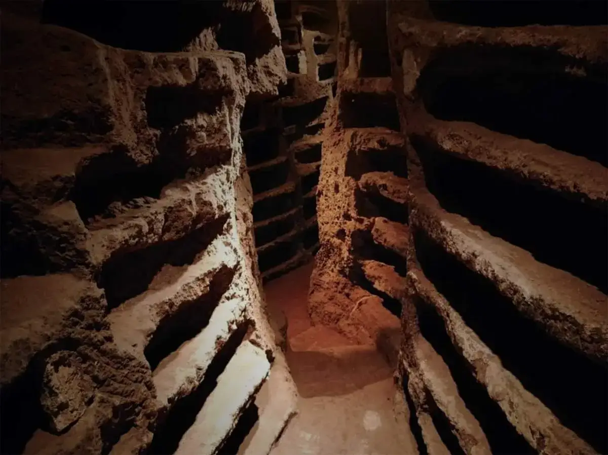 Passage étroit dans les catacombes Saint-Calixte, avec des niches creusées dans la roche pour les sépultures.